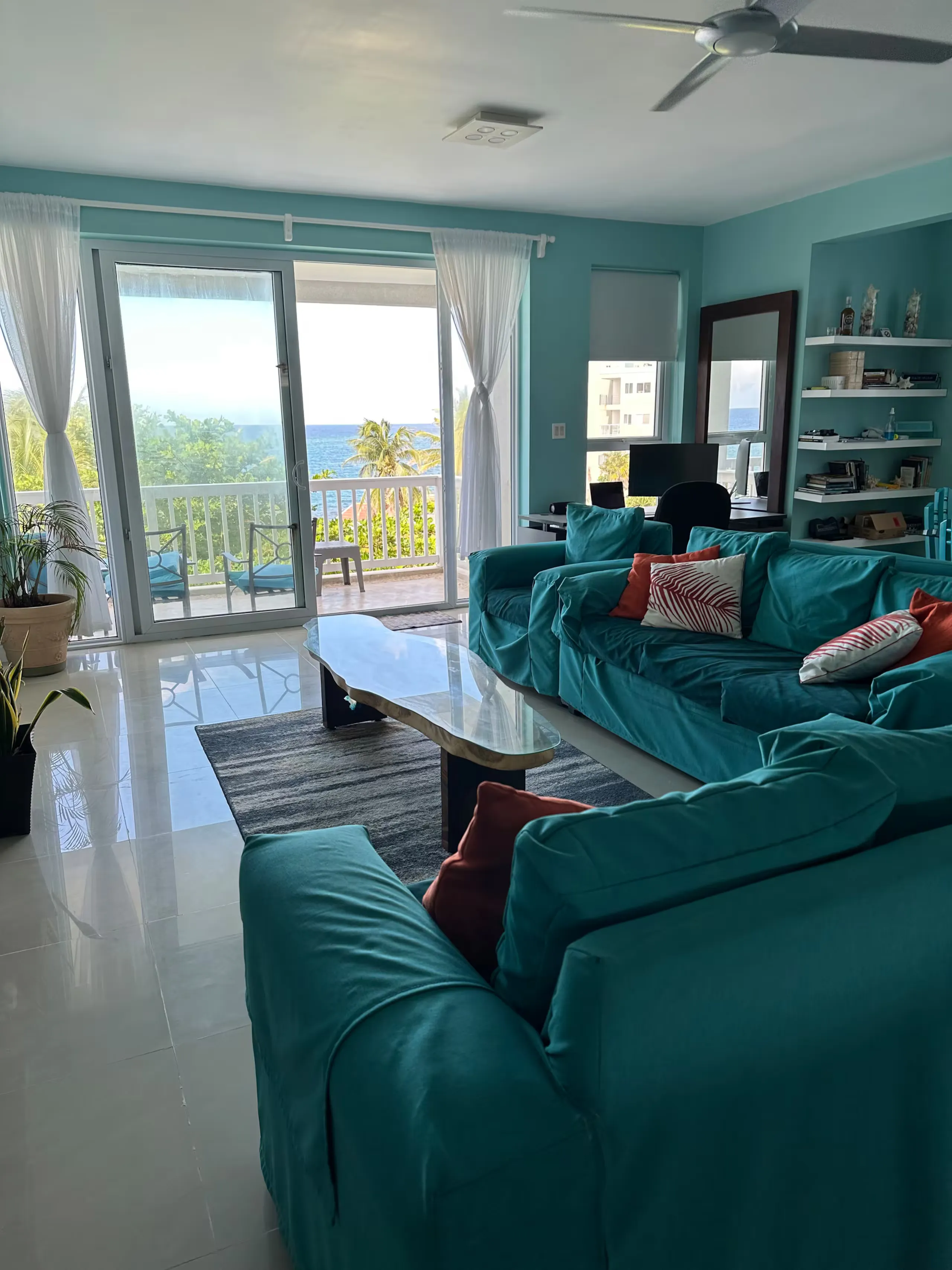 Open-plan living room with teal sofas and sliding glass doors onto the sea-view balcony.