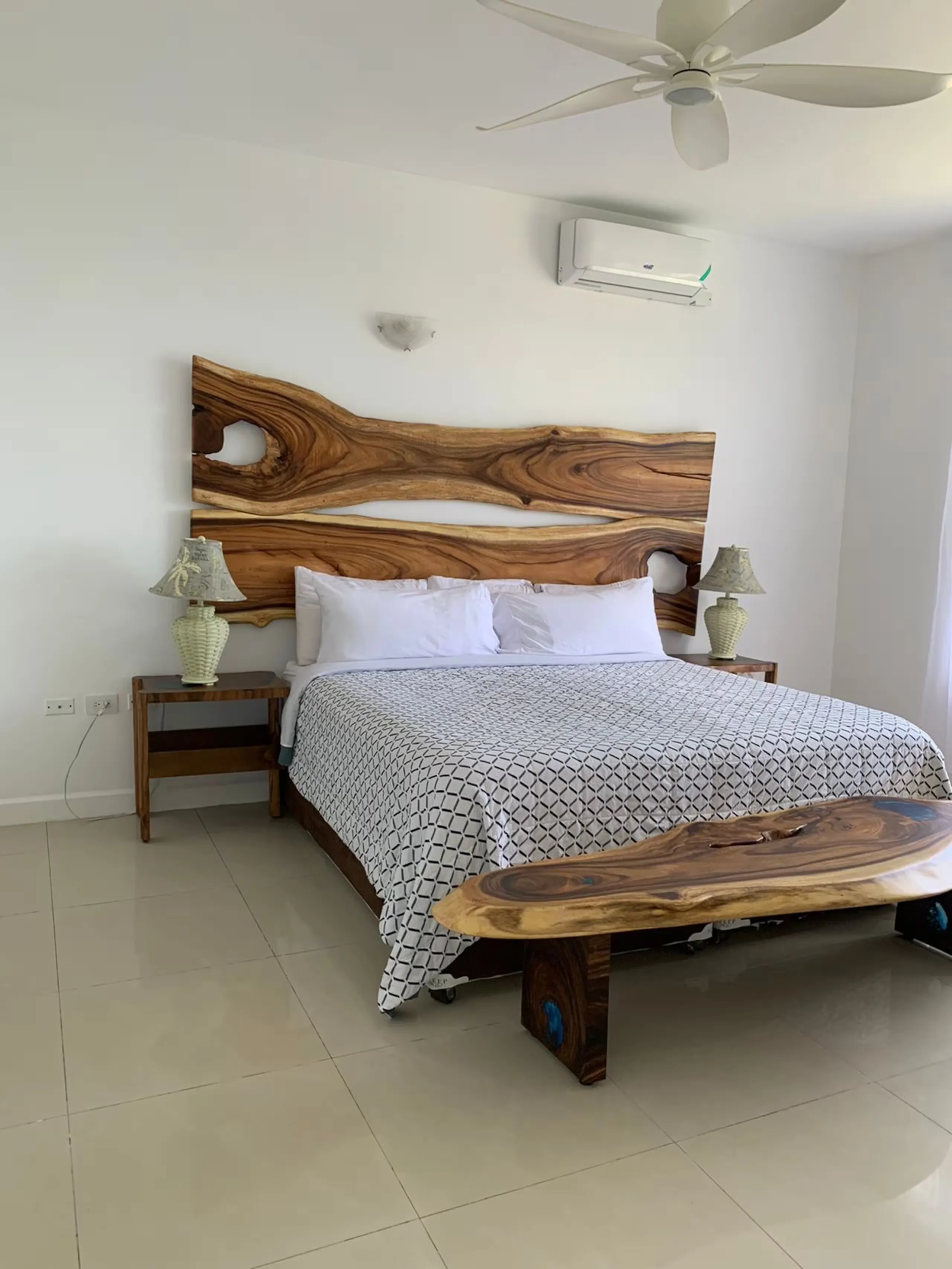 Primary bedroom with a live-edge wooden bed frame, air conditioning unit and a window to the sea.