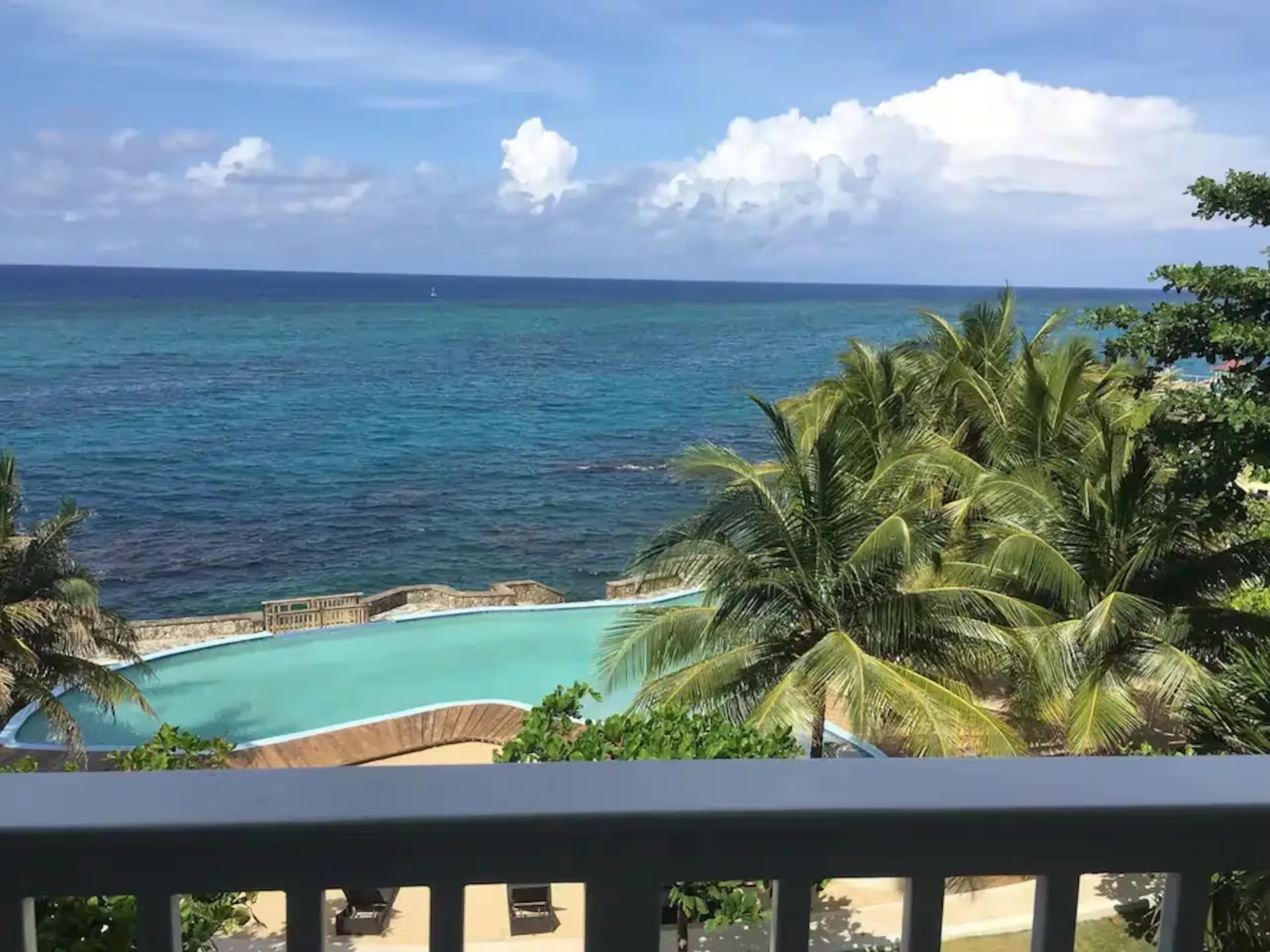 View from the balcony over the sea and the complex pool, framed by palms.