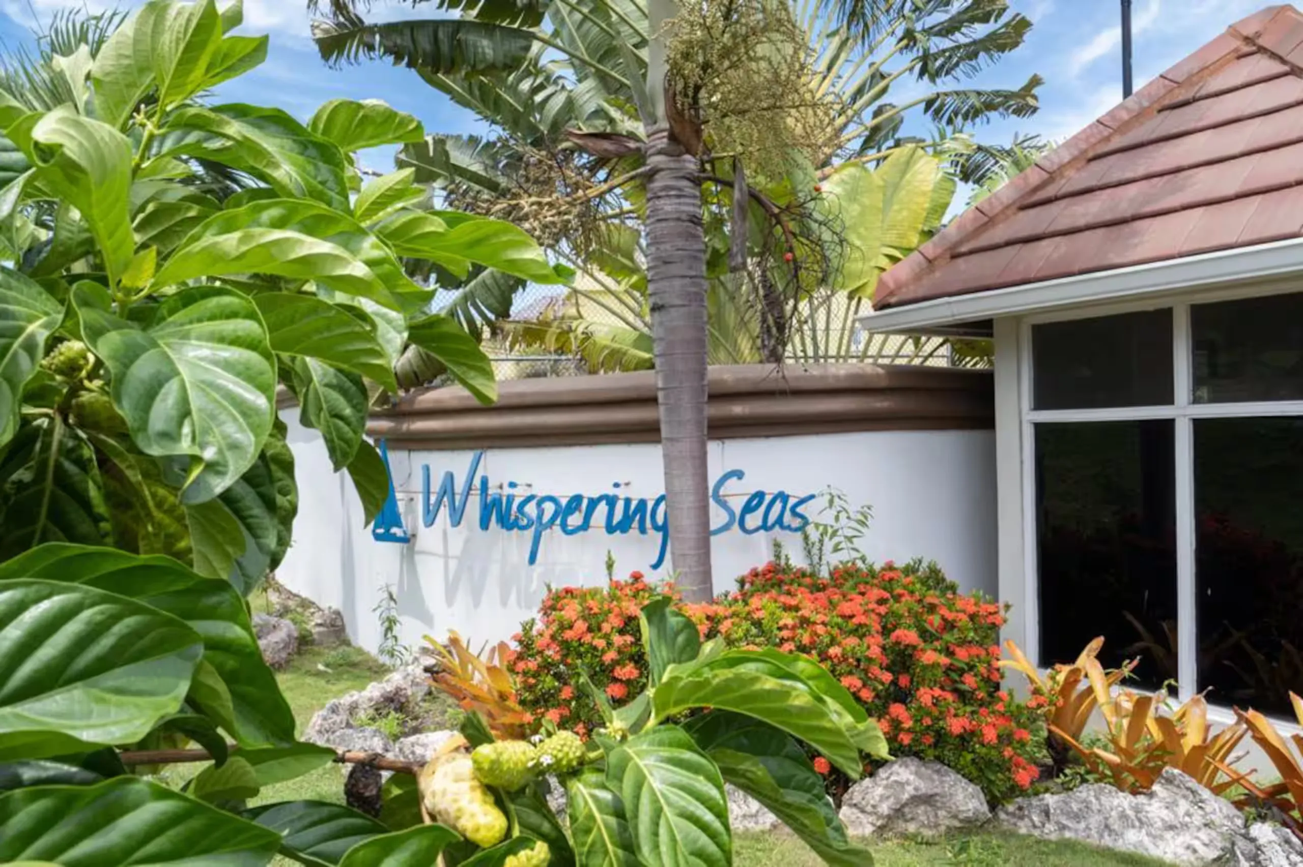 The carved 'Whispering Seas' sign set among tropical flowers at the entrance to the complex.