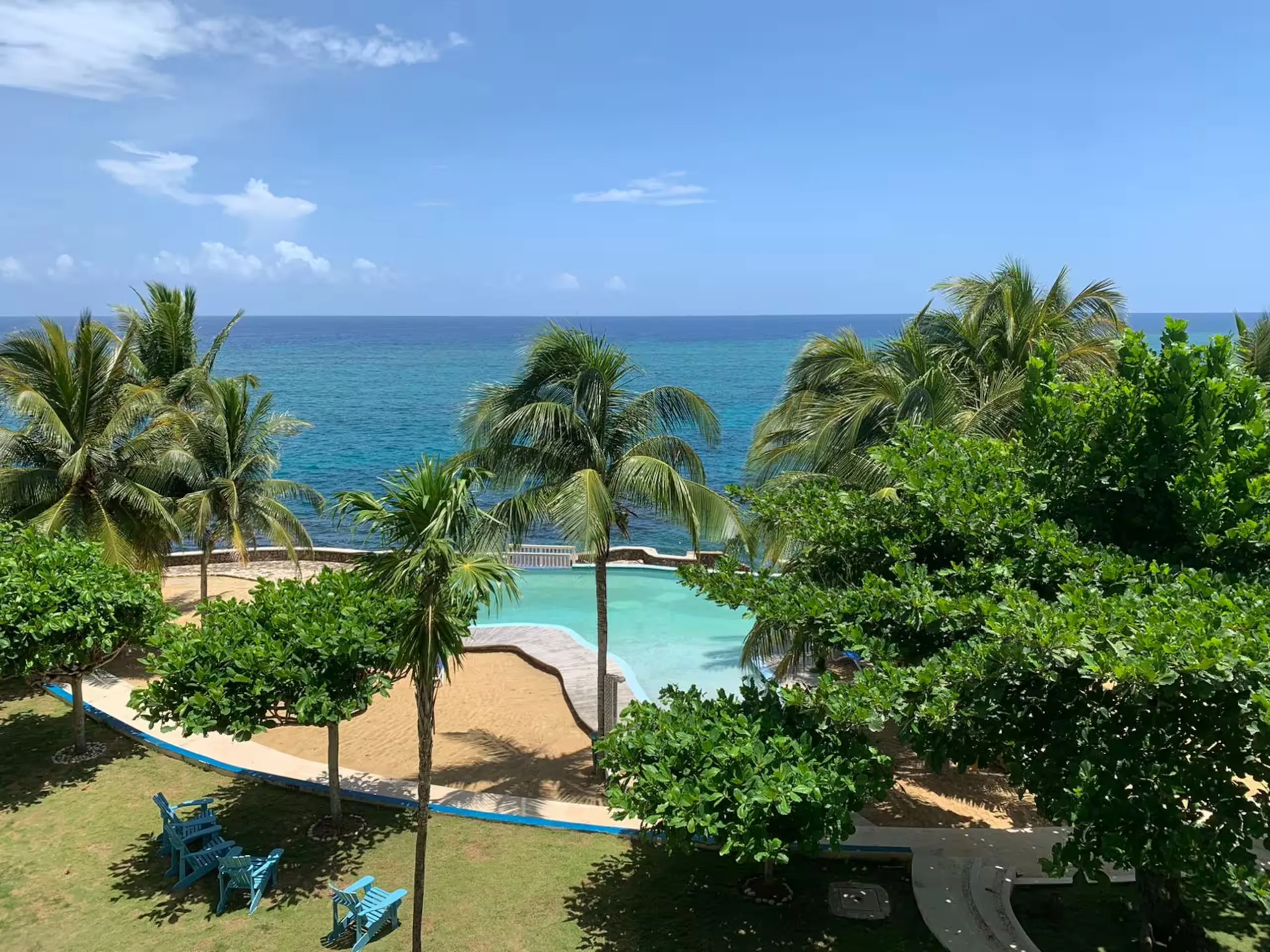 The pool and garden with the sea on the horizon, seen from above.