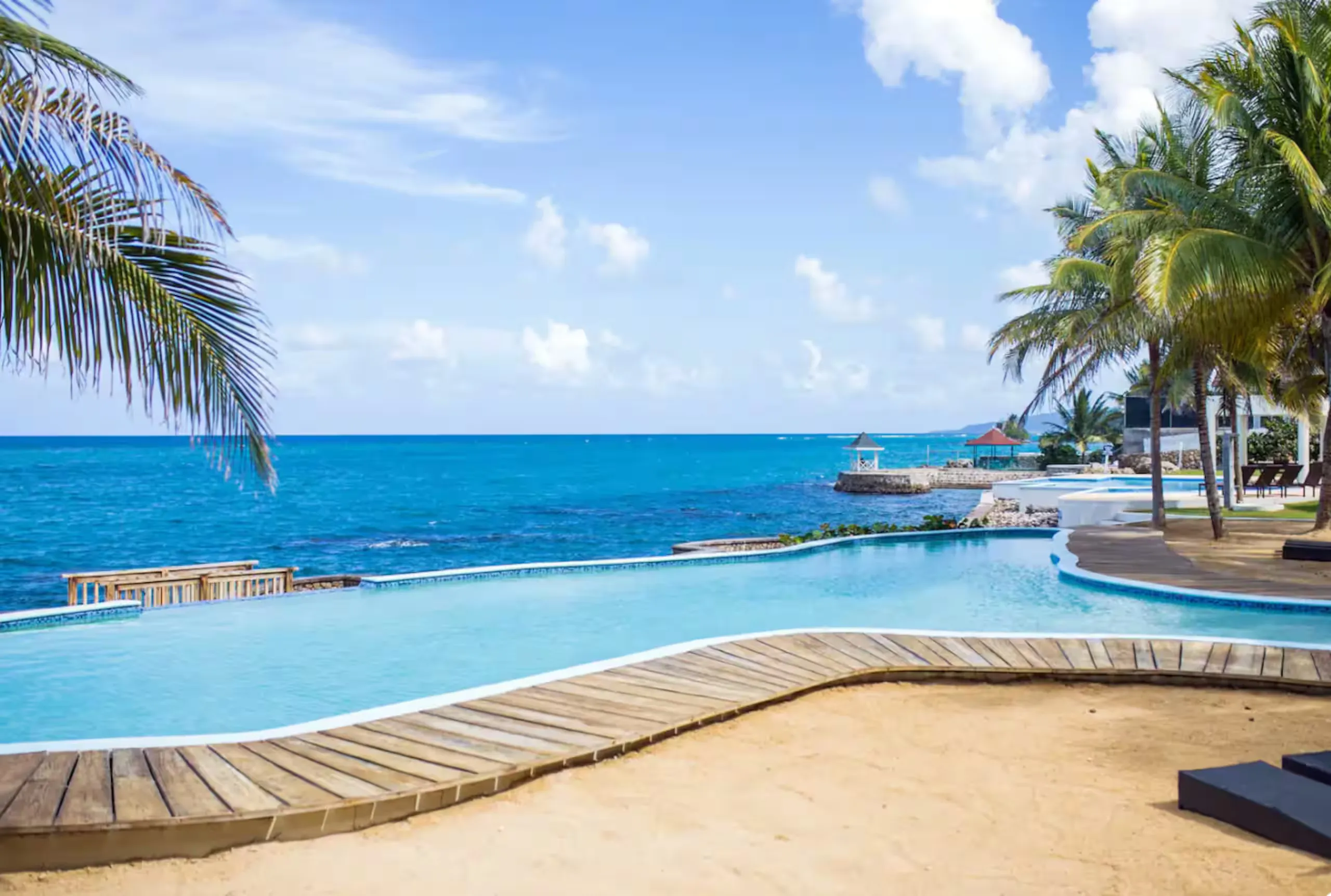 The shared sea-water pool with a wooden deck, palms and the open ocean behind.
